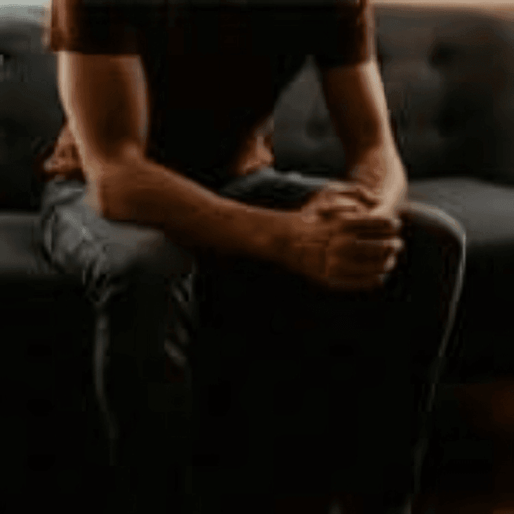 Illustration: A man sitting on a sofa, holding his palms together with fingers crossed, leaning on his hands resting on his thighs