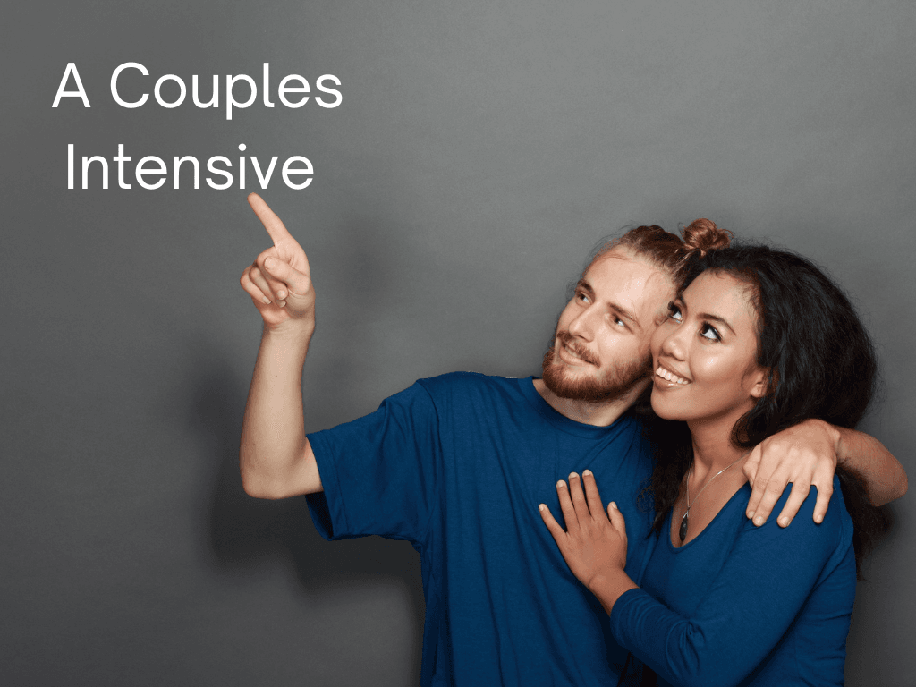 A happy couple wearing matching blue shirts stands against a gray background. The man has his arm around the woman and is pointing forward with a smile, while the woman looks at him affectionately. The text 'A Couples Intensive' is displayed on the left side of the image.